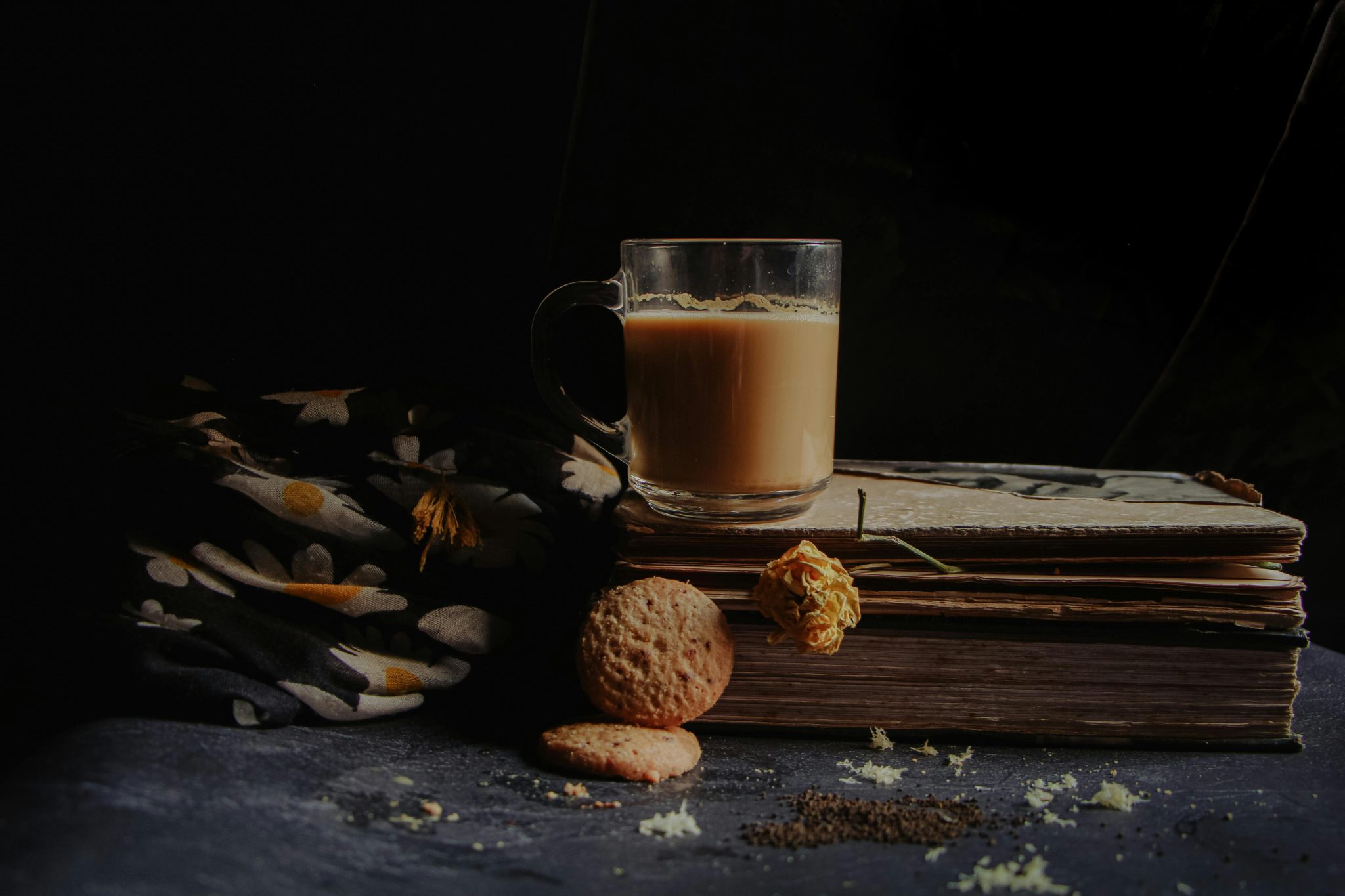 A cozy still life of tea, cookies, and vintage books in low light, evoking warmth and nostalgia.